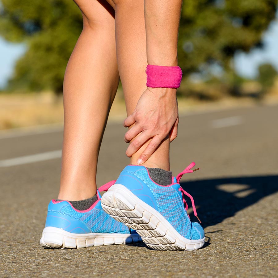 Runner holding her ankle in pain during a run on the road